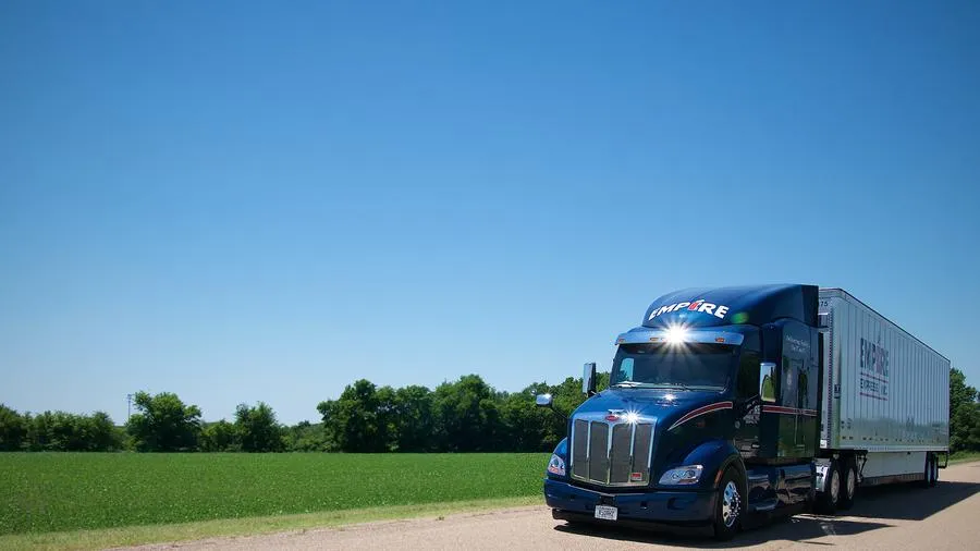 An Empire Express Peterbilt dry van tractor-trailer on a country road under a clear blue sky